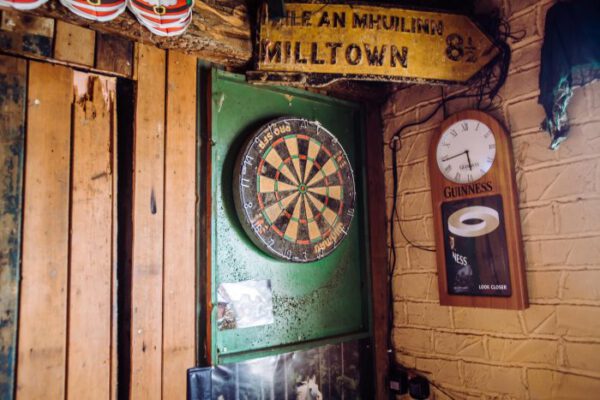 A dartboard and clock on the timber-panelled wall beside an old Milltown road sign