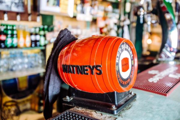 An orange Watneys barrel sitting on the bar counter in front of the bottle shelves