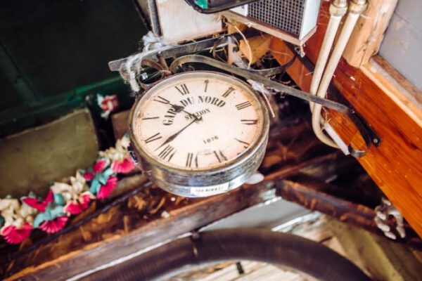 An old mantel clock on a dark shelf among decorations