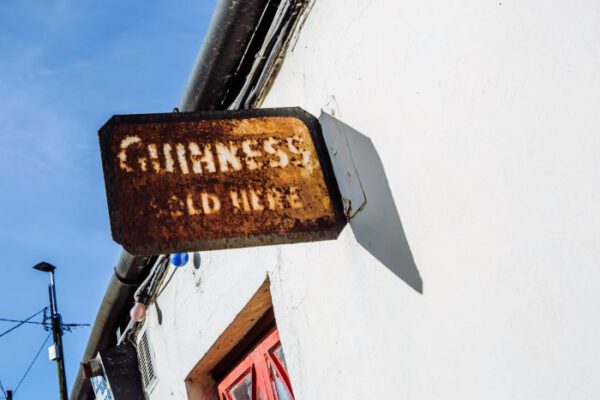 An old enamel Guinness sign hanging outside against the sky